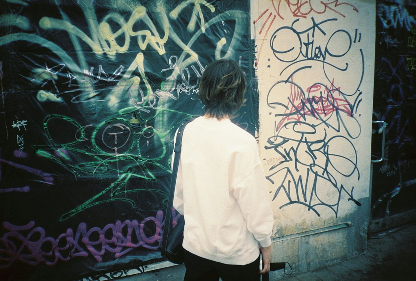 Persona de pie frente a una pared cubierta de grafitis coloridos.