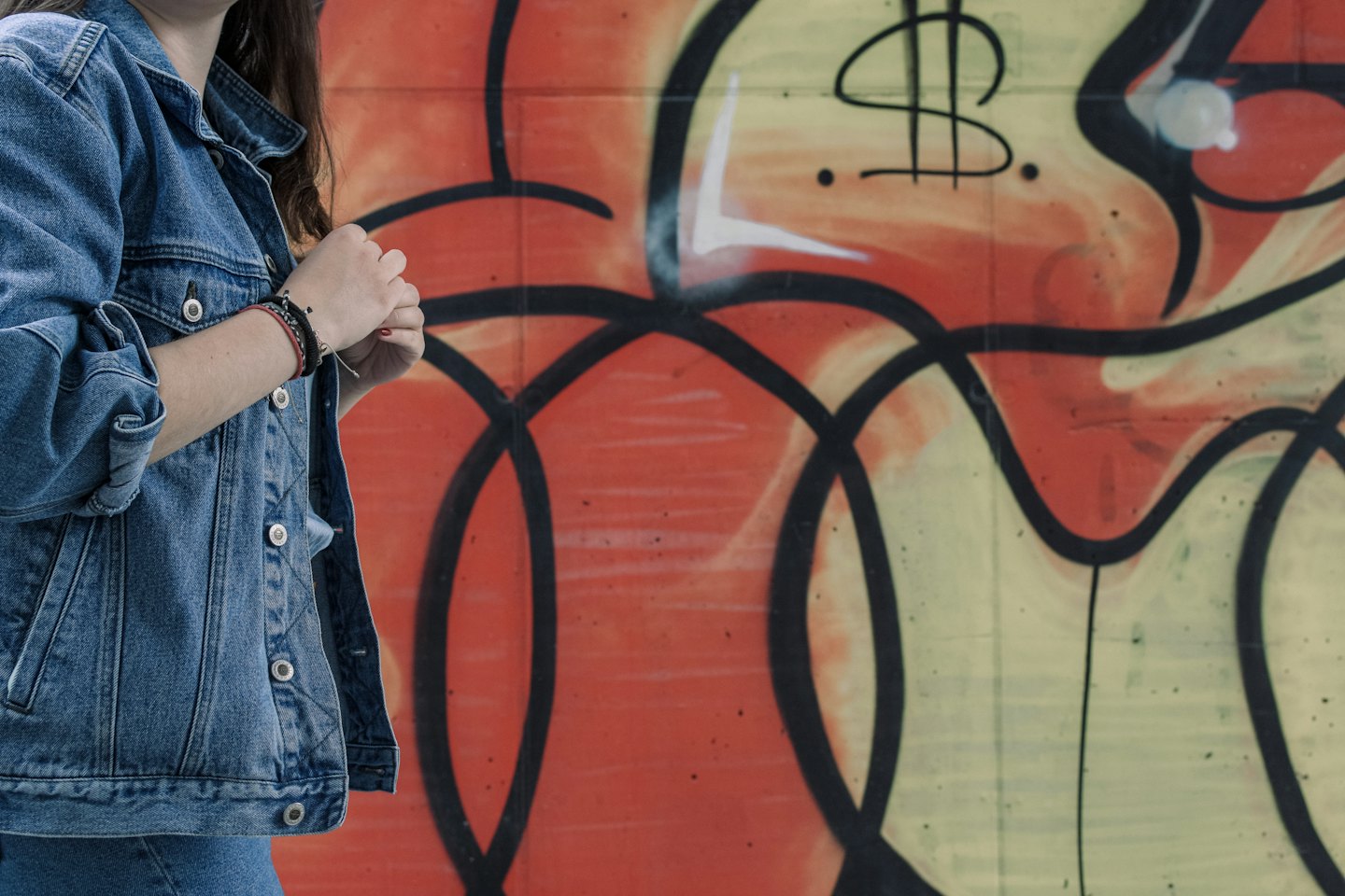 Una persona con chaqueta vaquera delante de una pared con grafitis.