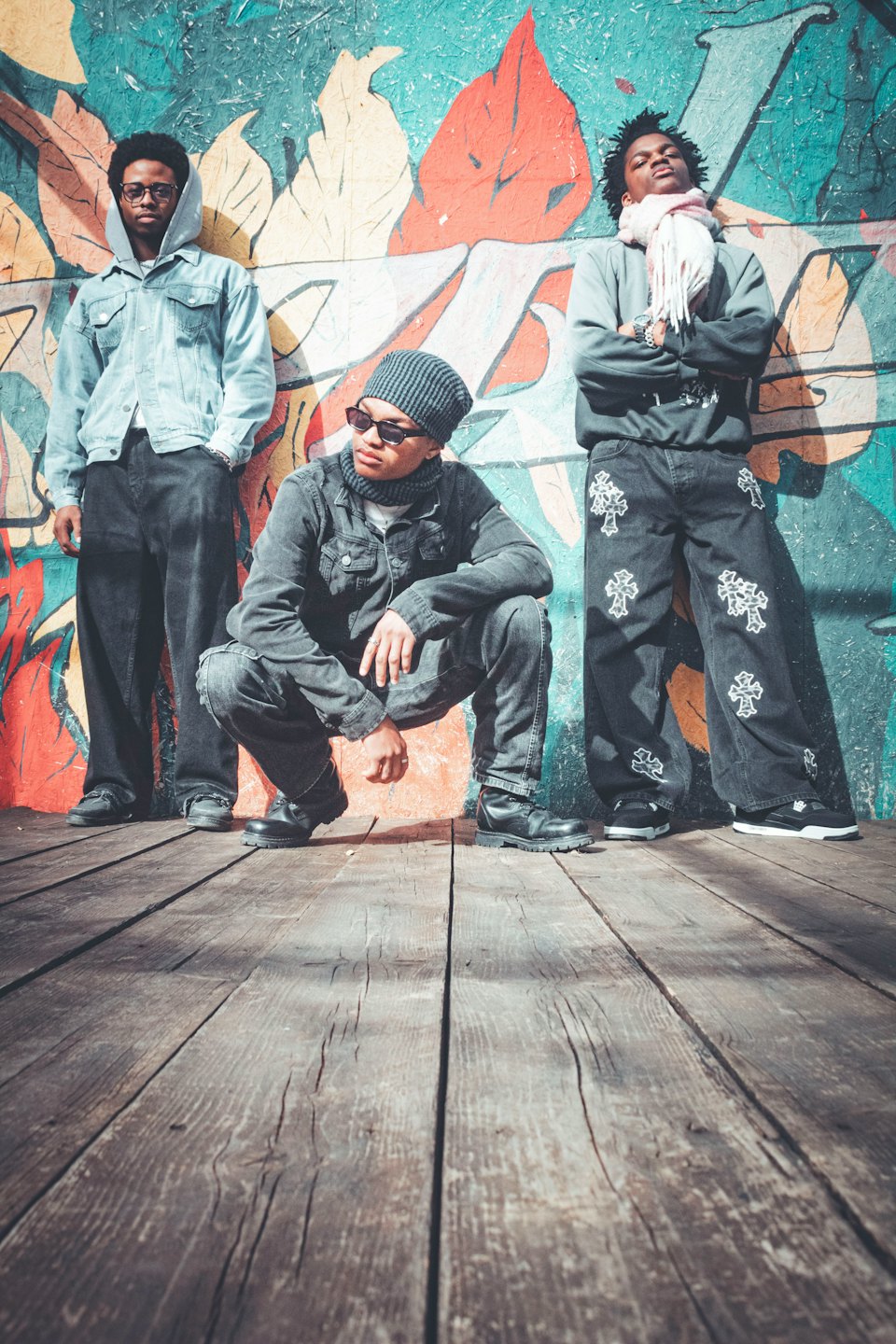 Tres hombres posando con ropa urbana frente a una pared con grafitis.