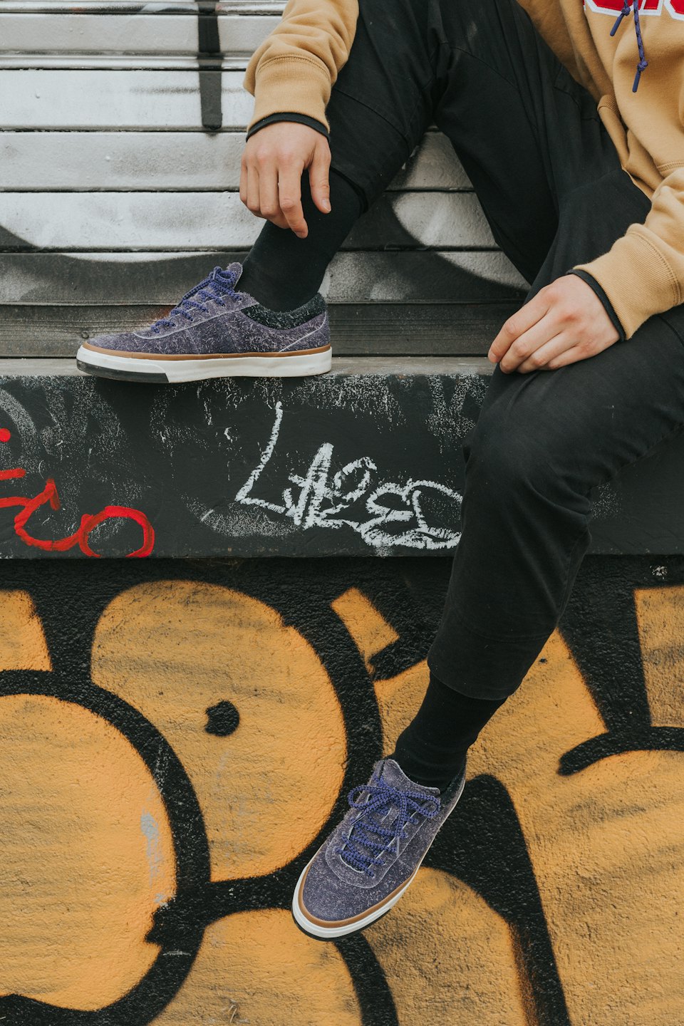 Persona en una cornisa cubierta de grafitis con zapatillas estampadas.